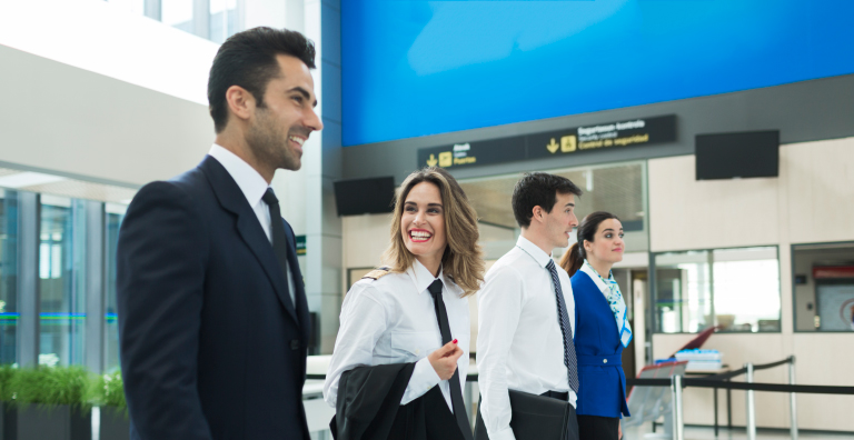 Four airport employees stand in a line smiling in an airport.